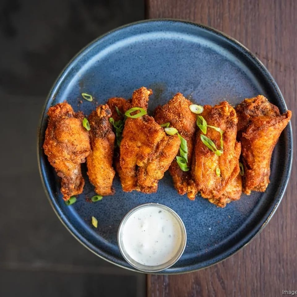 Crispy fried chicken wings, garnished with green onions, served with a side of ranch dressing.