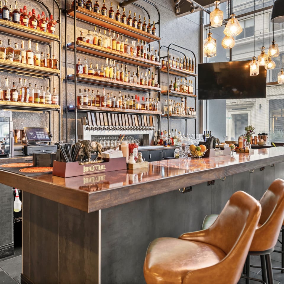A well-stocked bar with numerous liquor bottles on shelves, a long counter, and bar stools.