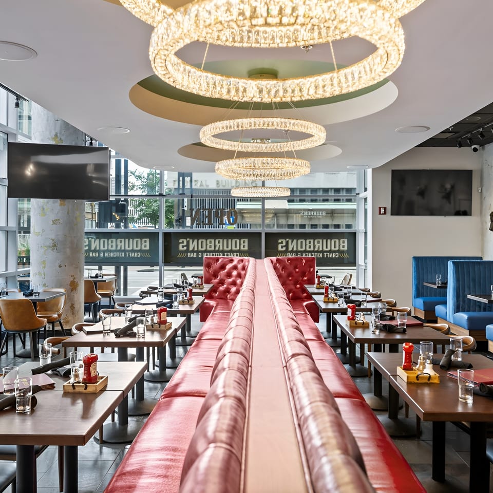 Spacious upscale restaurant interior with red and blue booths, set tables, large windows, crystal chandeliers, and colorful animal-head wall decor.