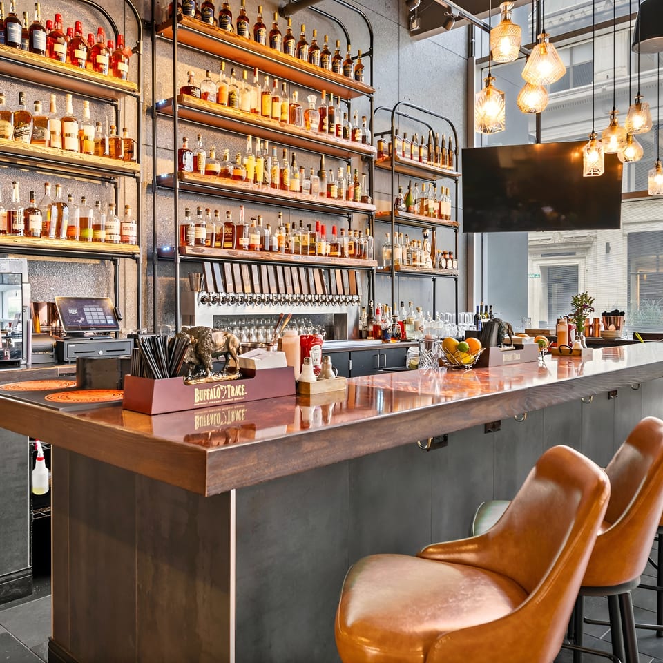 Stylish restaurant bar with liquor-filled shelves, beer taps, pendant lights, polished counter, and rows of leather stools.