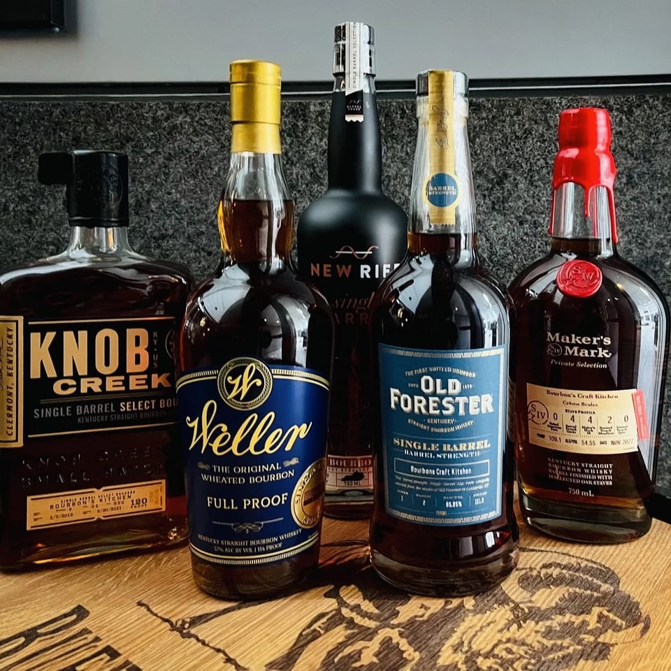 Five bottles of bourbon, including Knob Creek, Weller, New Riff, Old Forester, and Maker's Mark.