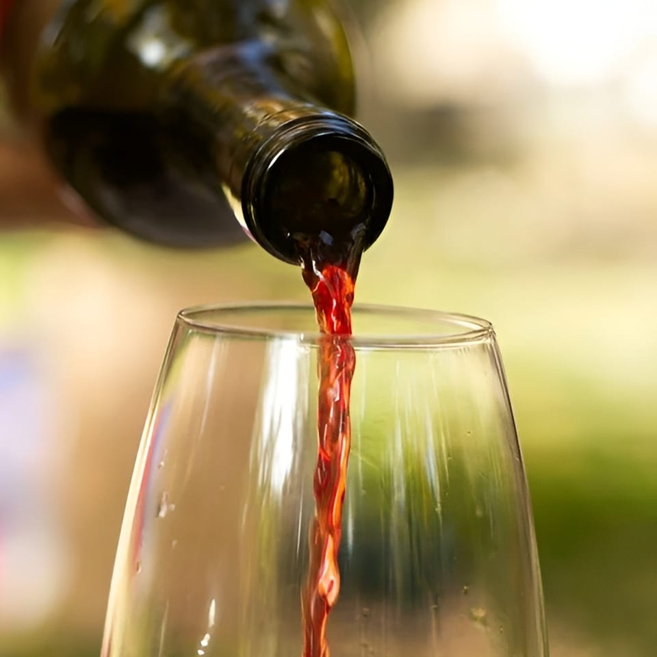 Red wine pours from a dark bottle into a clear wine glass against a softly blurred background.