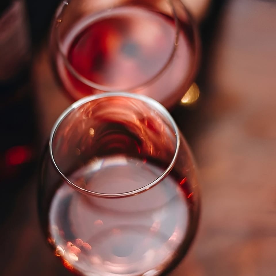 Two stemless glasses filled with red wine sit on a reflective table in warm, dim restaurant lighting.