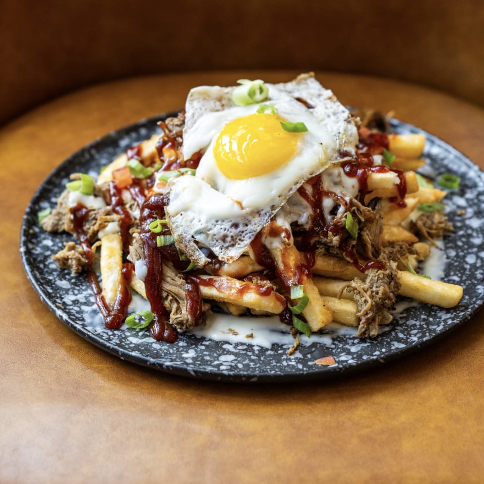 Loaded fries topped with pulled pork, BBQ sauce, white sauce, green onions, and a fried egg.