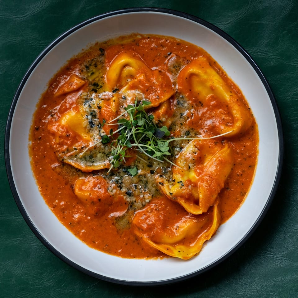 Filled pasta in orange sauce topped with grated cheese and microgreens.