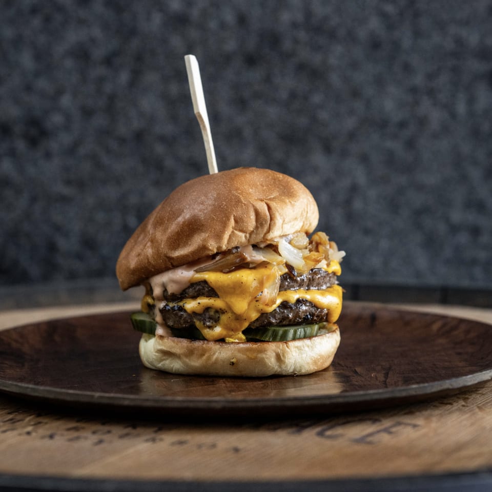Double cheeseburger with melted cheese, caramelized onions, and pickles on a wooden plate.